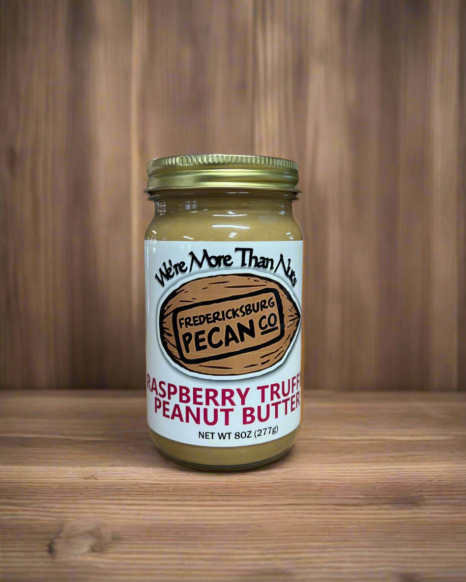 Jar of raspberry true pecan peanut butter on a wooden surface with a blurred kitchen background