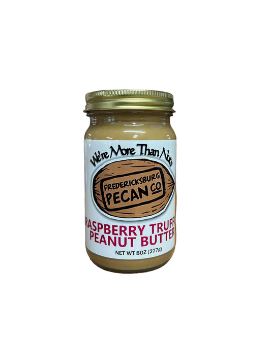 Jar of raspberry true pecan peanut butter on a wooden surface with a blurred kitchen background